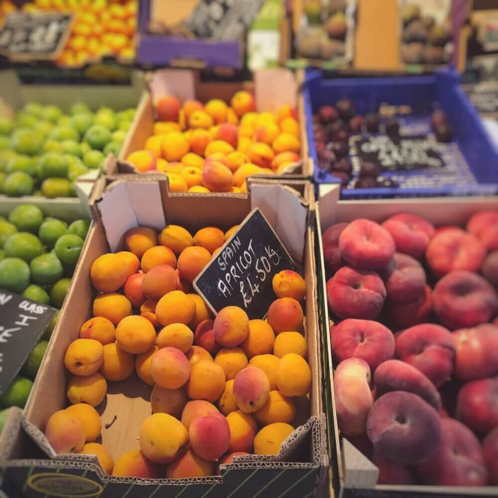 Boxes of assorted fruits, including apricots, peaches, and plums, displayed at a market with price tags on some. - Home Instead