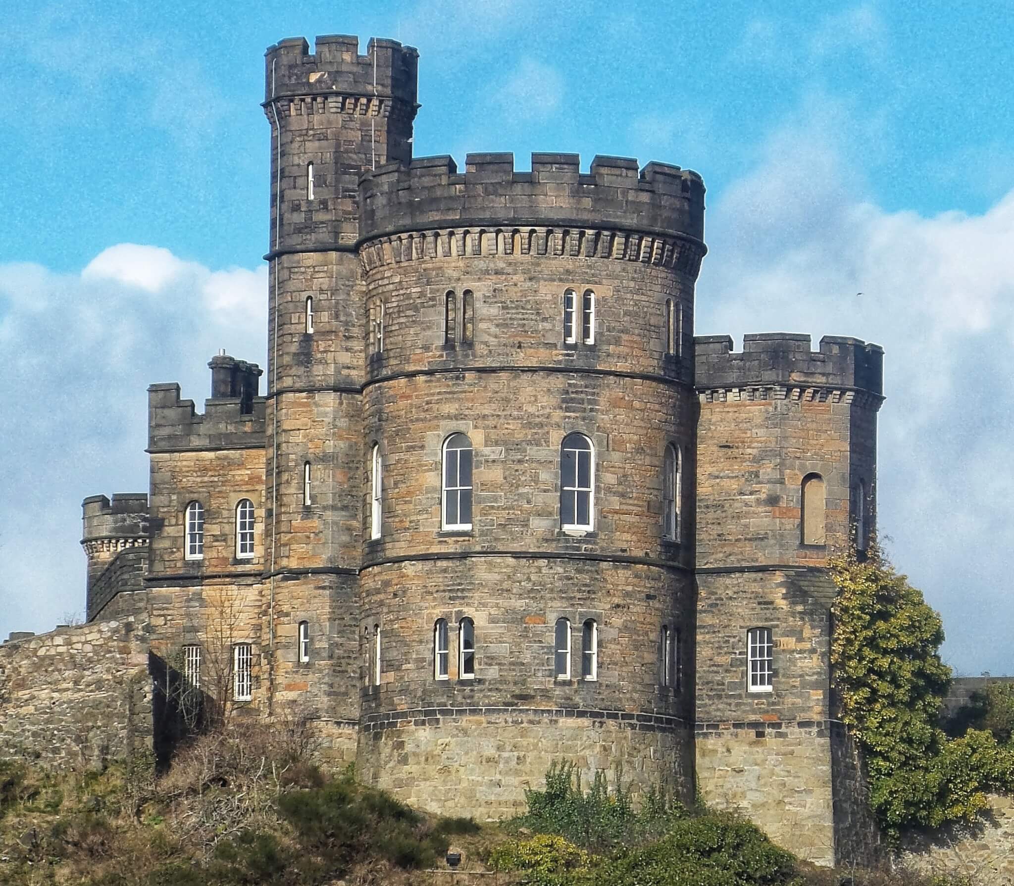 A historic stone castle with circular towers under a bright blue sky on a partly cloudy day. - Home Instead