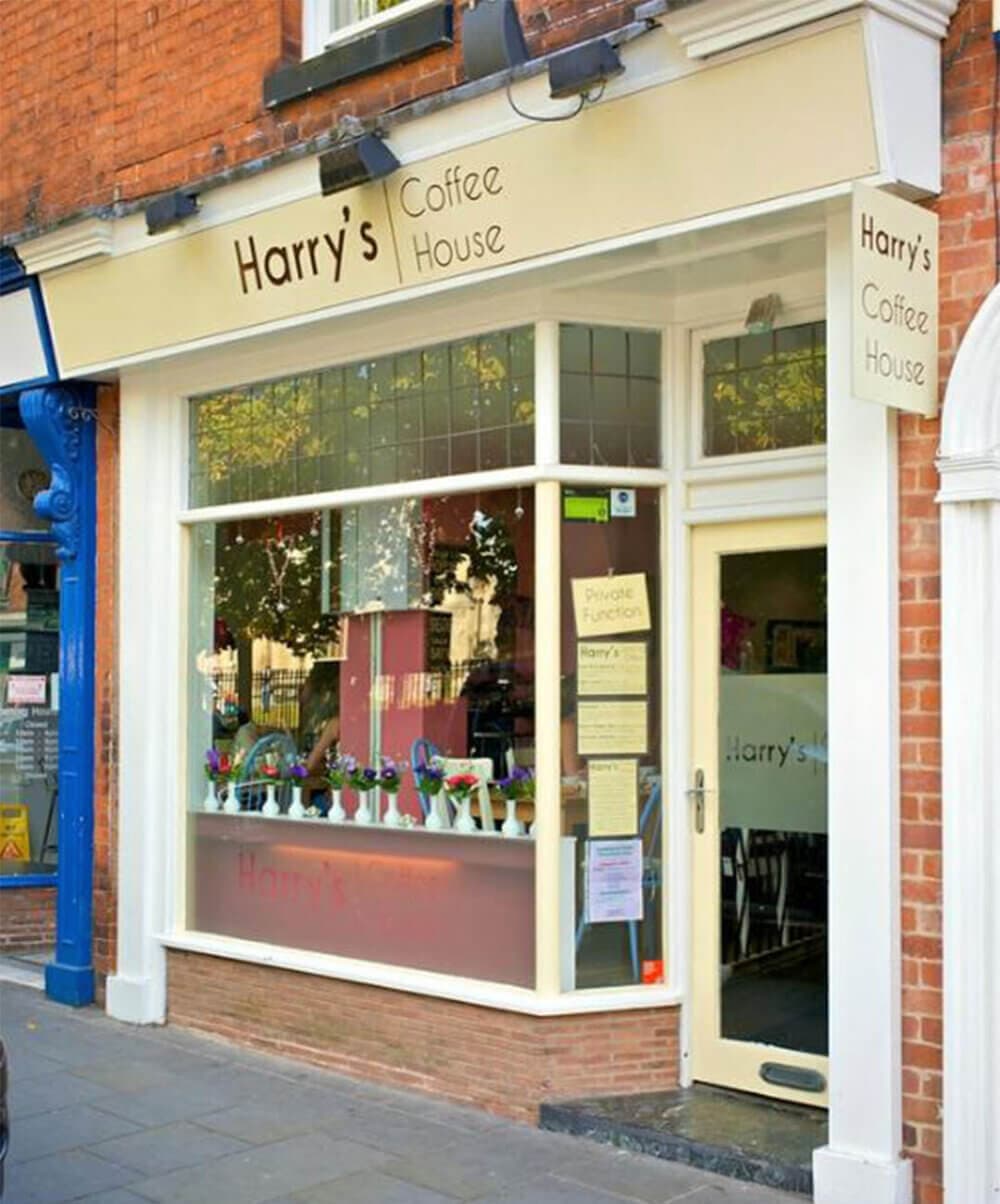 Front view of Harry's Coffee House with large window, door, and sign on a brick building. - Home Instead