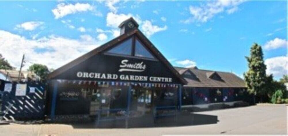 A garden center with a sign reading "Smith's Orchard Garden Centre" on a sunny day with a clear blue sky. - Home Instead