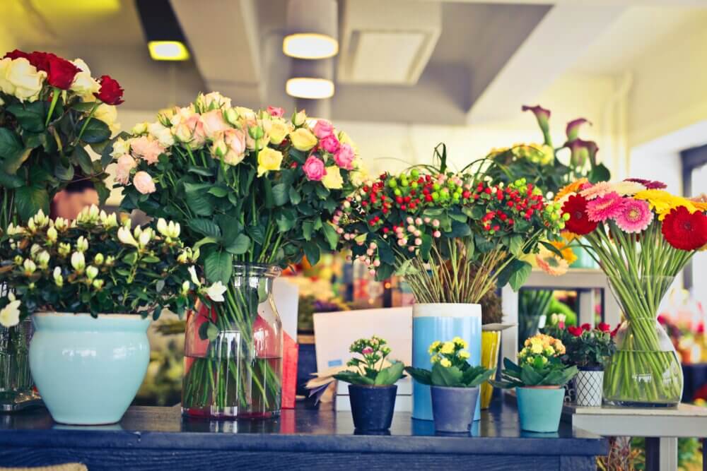 A colorful display of various flowers in vases and pots on a counter in a flower shop. - Home Instead
