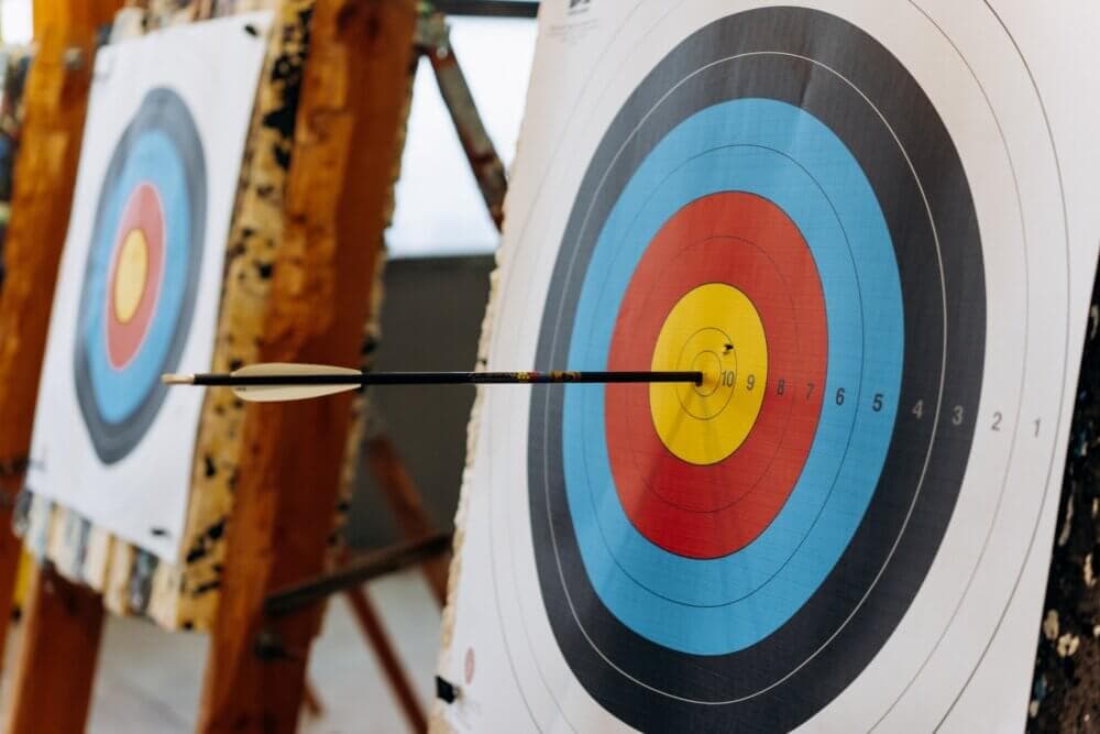 A close-up of a target with concentric circles, showing an arrow that has hit the bullseye. - Home Instead