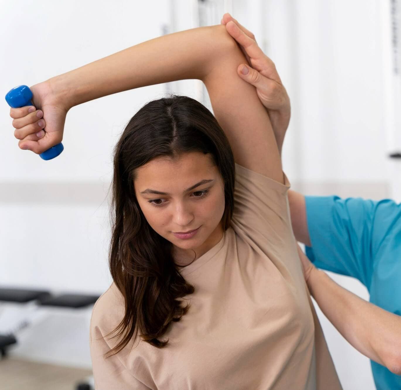 A woman is lifting a dumbbell above her head with assistance from a trainer's hand supporting her arm. - Home Instead