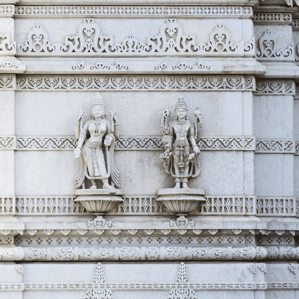 Two intricate stone statues of deities on an ornate temple wall, with detailed carvings and patterns surrounding them. - Home Instead