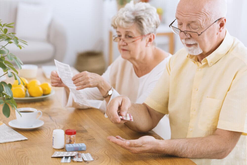 Elderly couple sitting at a table, reading medication instructions and dispensing pills. - Home Instead