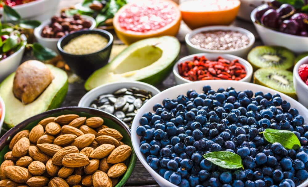A vibrant array of superfoods, including blueberries, almonds, avocado, seeds, and various fruits in bowls. - Home Instead