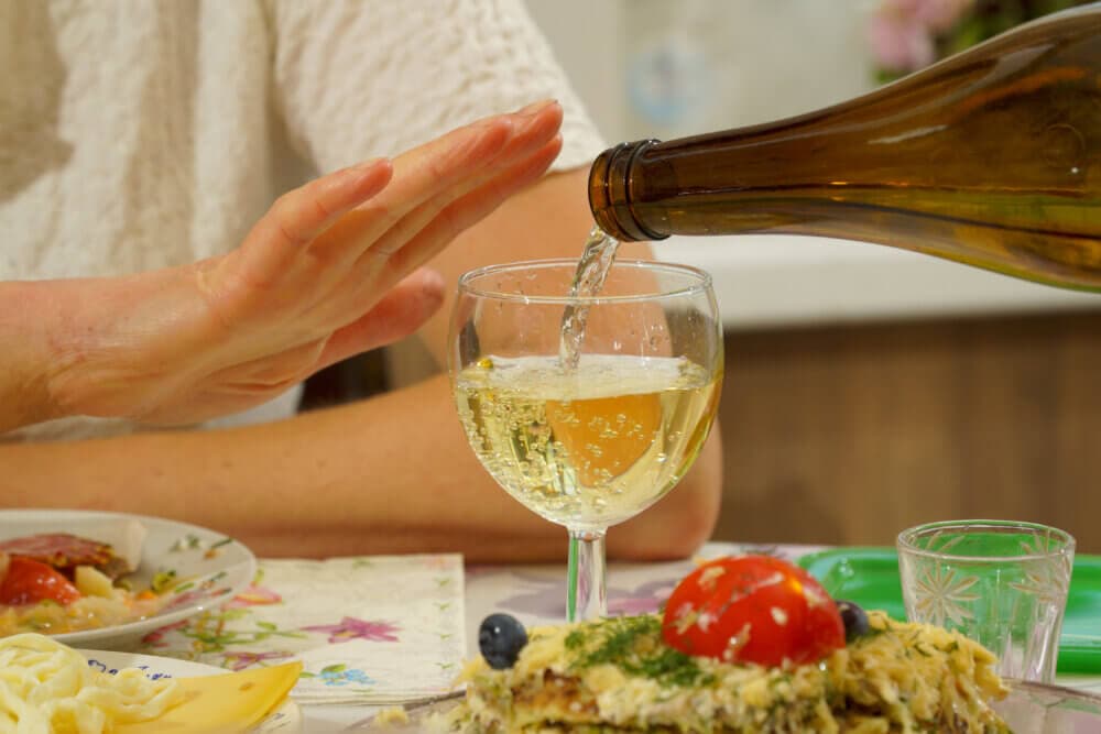 Person with their hand raised, signaling to stop, while someone pours a drink into a glass at a dining table. - Home Instead