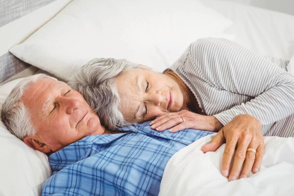 Elderly couple lying in bed, resting peacefully, with the woman’s head on the man’s shoulder. - Home Instead