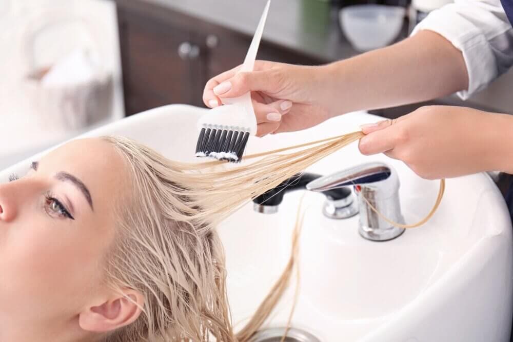 Person seated at a salon sink getting hair dye applied with a brush by a stylist. - Home Instead