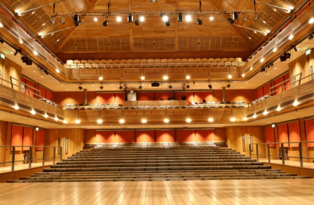 Empty, well-lit concert hall with wooden interior featuring tiered seating and balcony views. - Home Instead