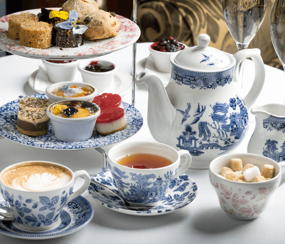 Afternoon tea setting with tiered tray of pastries, tea pot, tea cups, and coffee on a white tablecloth. - Home Instead