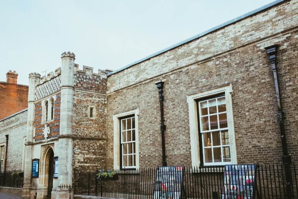 Historic brick building with a tall entrance tower, large windows, and a wrought-iron fence in front. - Home Instead