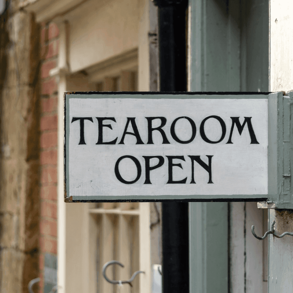 Sign reading "TEAROOM OPEN" outside a building with a blurred background. - Home Instead