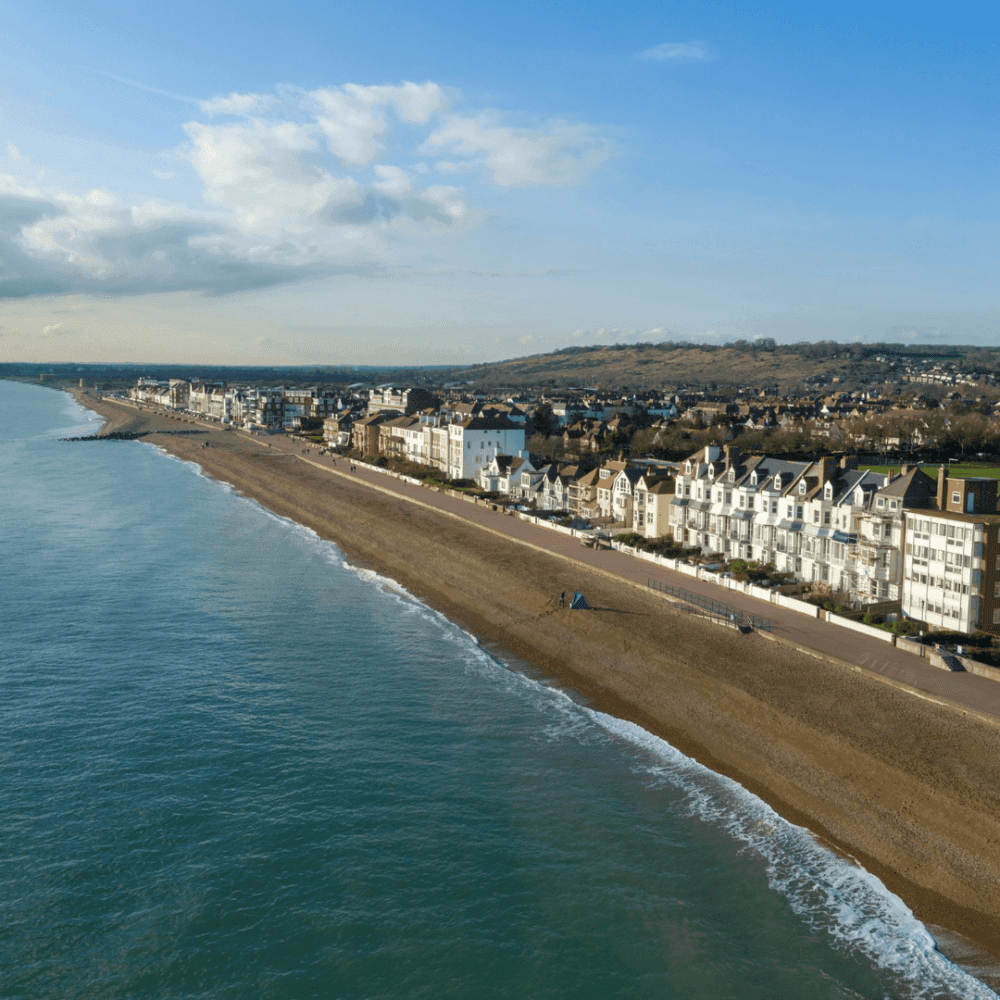 A coastal town with a beach, residential buildings, and hills in the background under a clear blue sky. - Home Instead