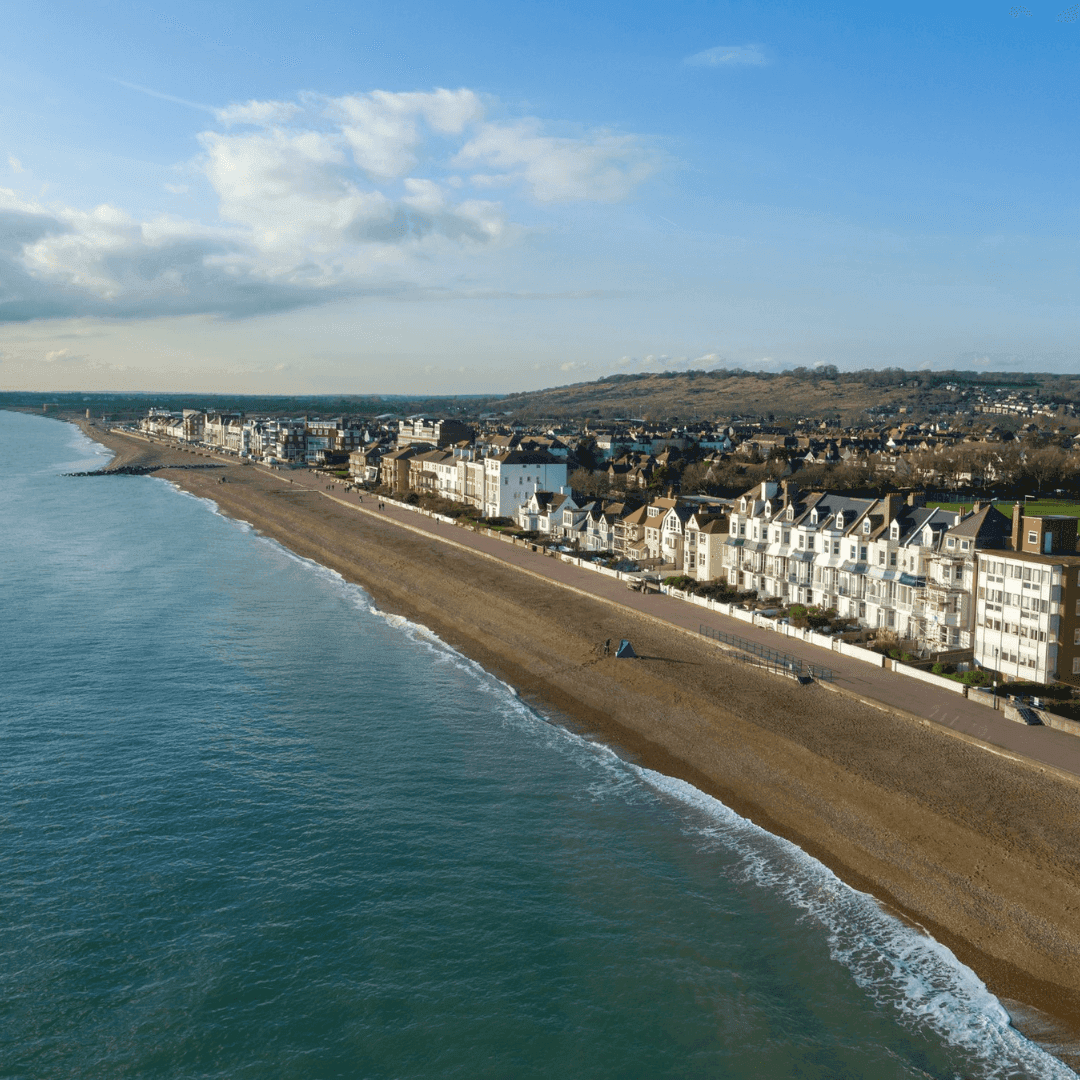 A coastal town with a beach, residential buildings, and hills in the background under a clear blue sky. - Home Instead