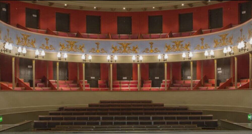 Empty classic theater with red and gold decor, balconies, and rows of seats. - Home Instead