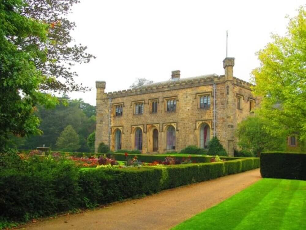 Historic stone building surrounded by lush gardens and a gravel pathway on a clear day. - Home Instead