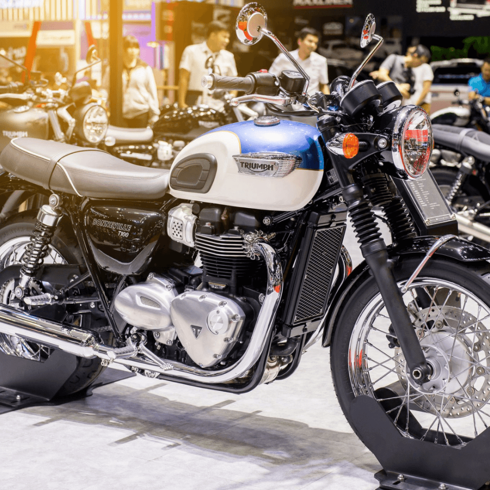 A Triumph Bonneville T120 motorcycle showcased at an exhibition, with people in the background. - Home Instead