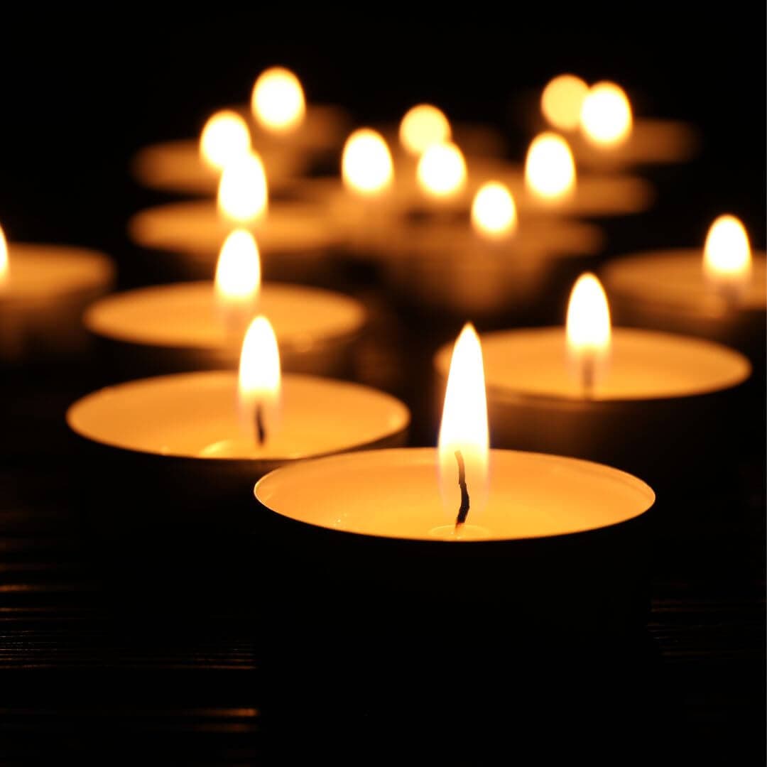 Several lit tea candles arranged in a group, creating a warm and calming glow in a dark environment. - Home Instead