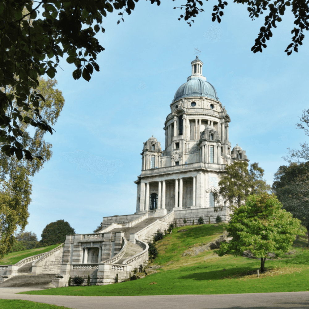 A grand, white-domed building with stairs and lush greenery, framed by tree branches against a clear sky. - Home Instead