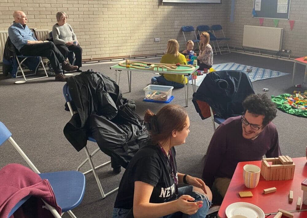 A group of people are sitting and playing with toys in a room. Some children and adults are interacting and playing. - Home Instead
