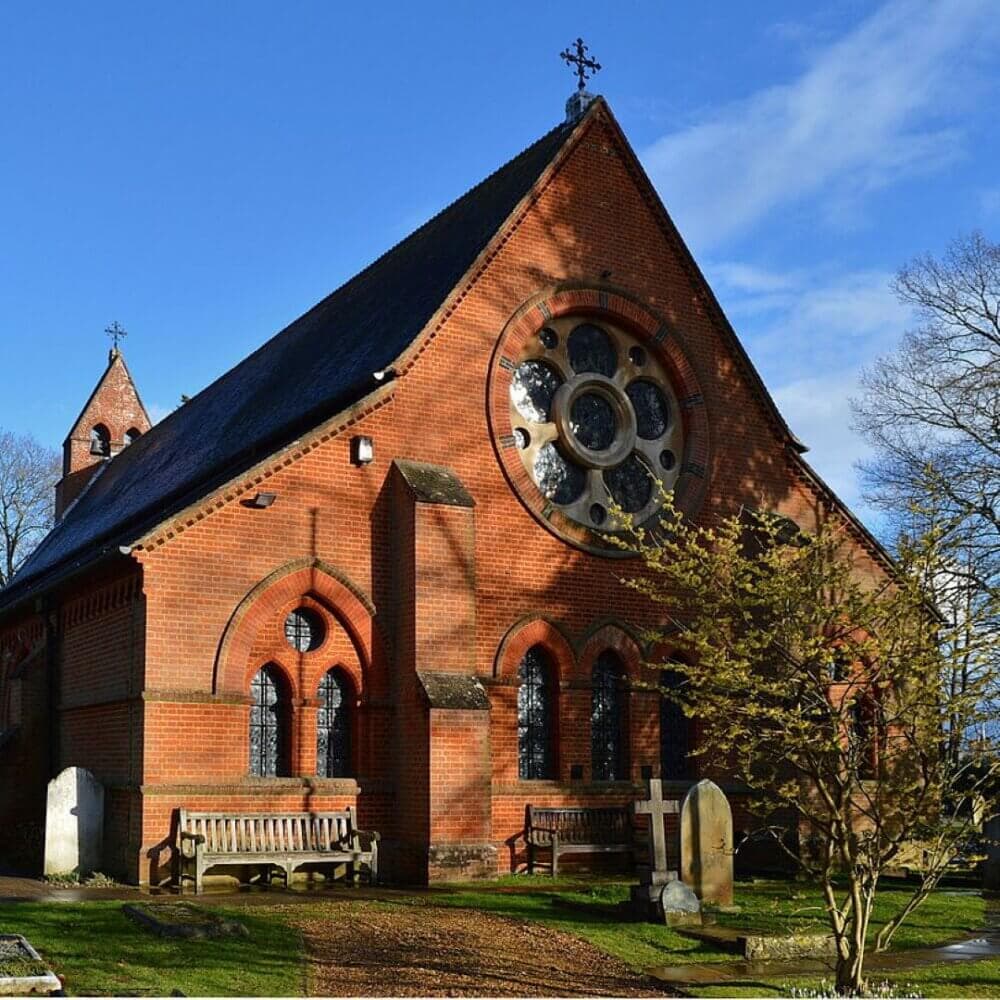 Red brick church with a large rose window, arched windows, and grave markers in front, set against a clear blue sky. - Home Instead