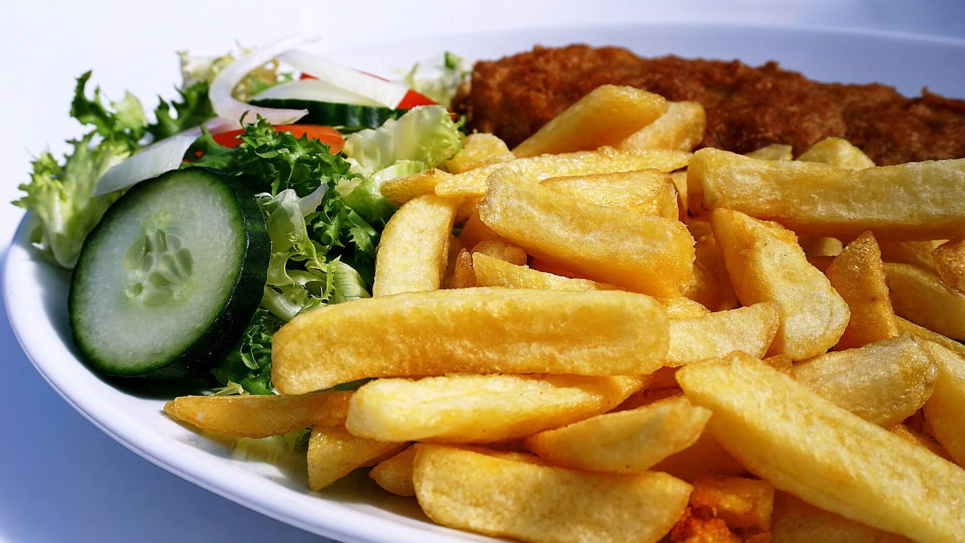 A plate of golden French fries, a green salad with lettuce, cucumber, onions, and a piece of breaded fried fish. - Home Instead