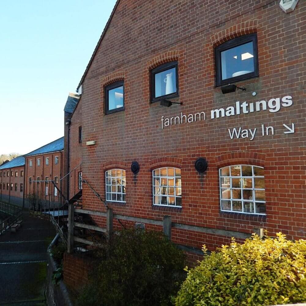 Brick building exterior with sign reading "Farnham Maltings" and "Way In," highlighting the entrance direction. - Home Instead