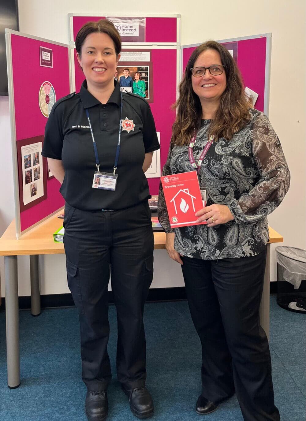 Two people standing in front of a display board; one is in a uniform and the other is holding a red booklet. - Home Instead