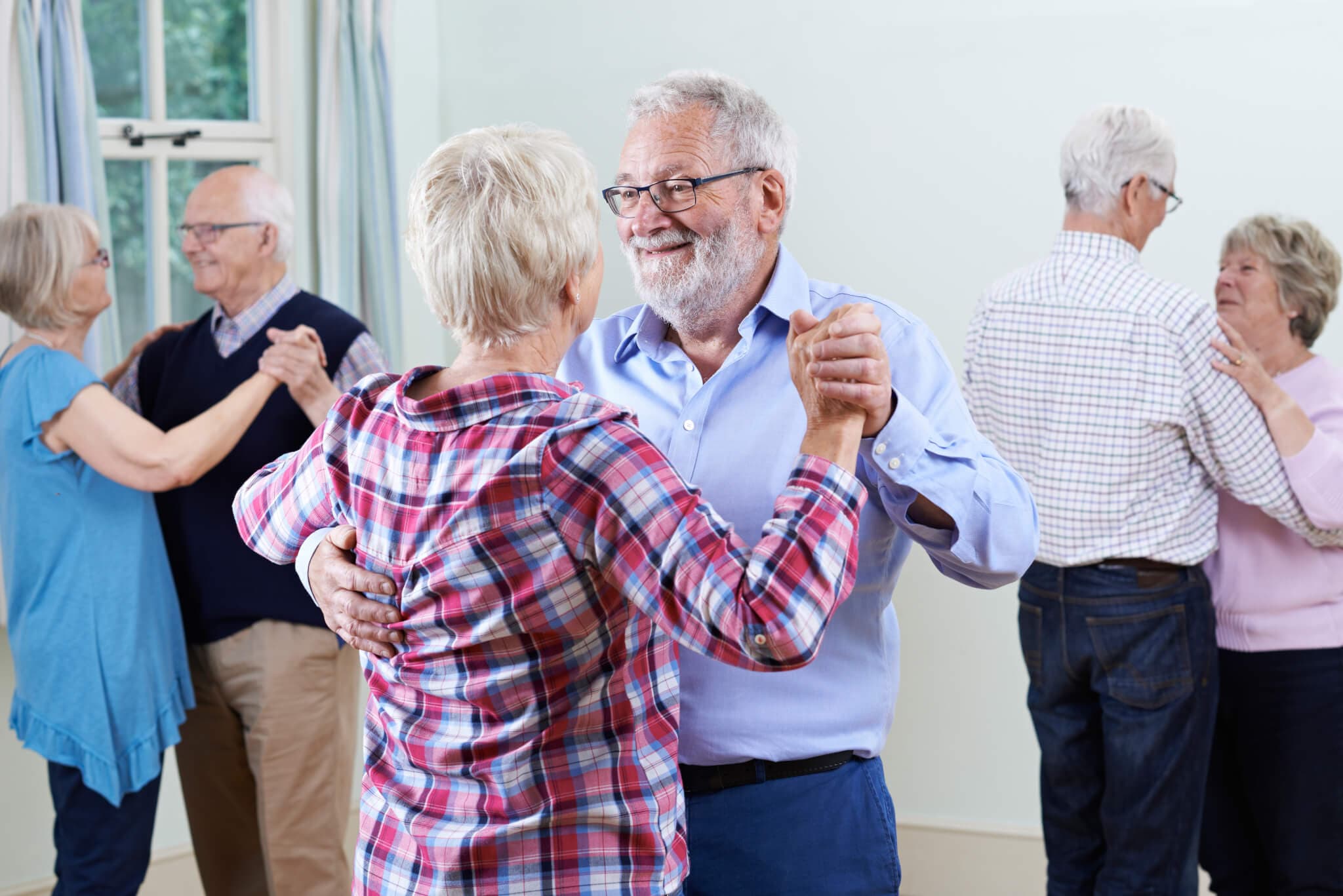 Older couples smiling and dancing in a bright room, enjoying each other's company. - Home Instead