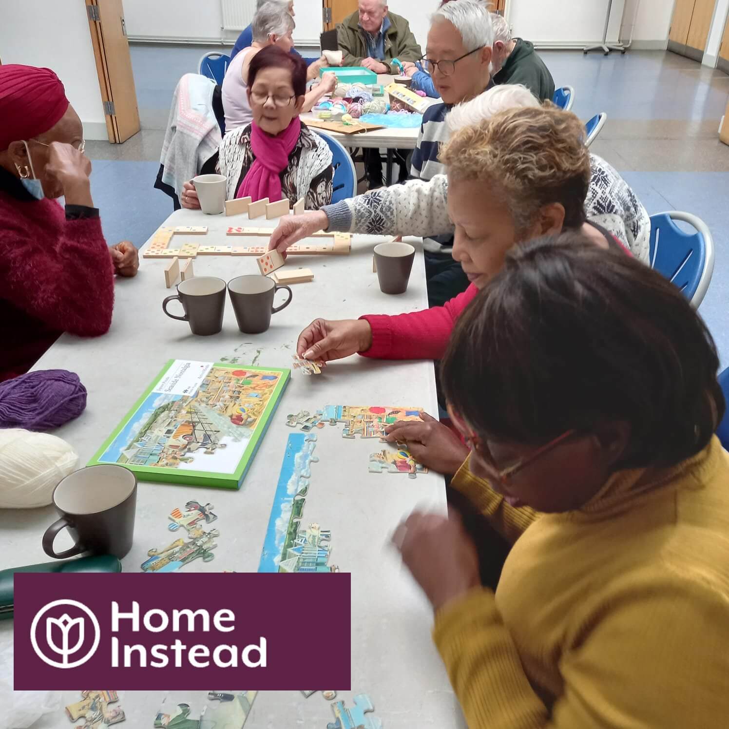 A group of elderly people gathered around a table working on a puzzle, with a "Home Instead" logo at the bottom left. - Home Instead