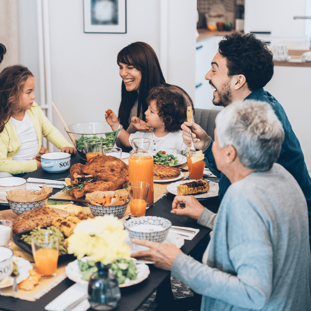 Family sharing a joyful meal at a dining table filled with various dishes, including a roast chicken and salads. - Home Instead