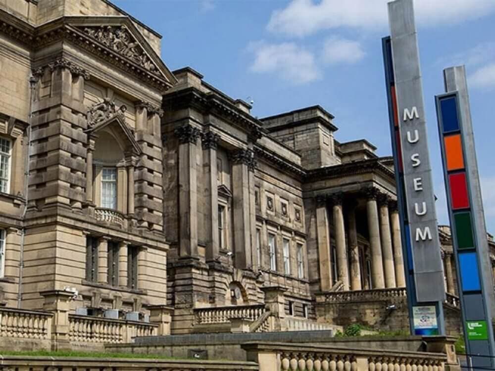 Large historic building with columns and ornate details, next to a modern sign reading "MUSEUM" in colorful letters. - Home Instead