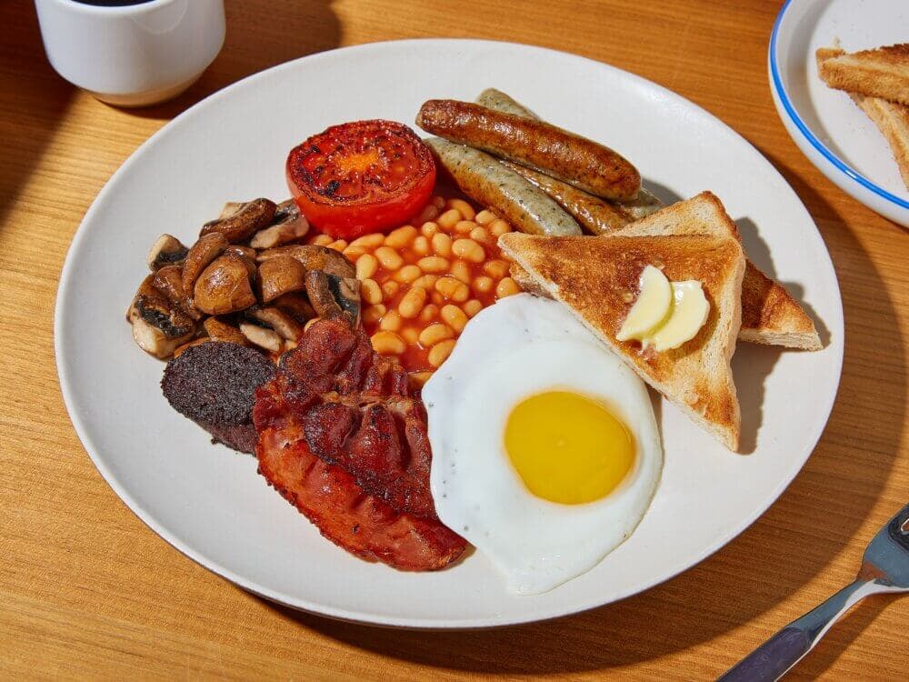 A plate with an English breakfast: egg, bacon, sausages, baked beans, mushrooms, grilled tomato, black pudding, and toast. - Home Instead