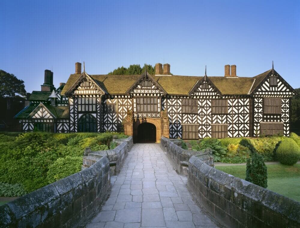 Historic timber-framed house with a stone pathway leading to the entrance, surrounded by lush greenery. - Home Instead