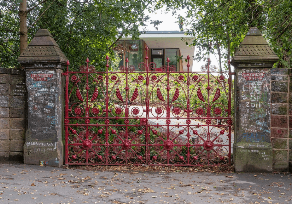 Red ornate iron gate in front of a house, with brick pillars covered in graffiti and surrounded by trees. - Home Instead