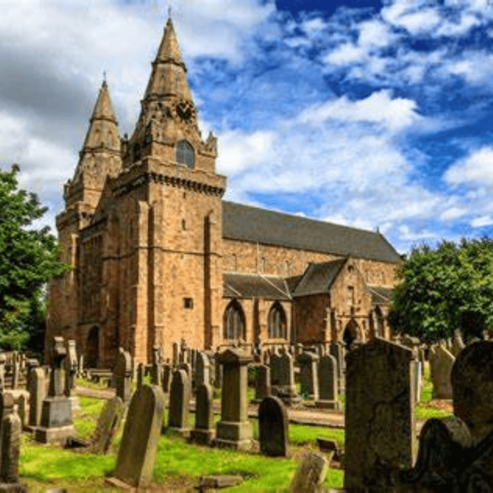 Historic stone church with two towers and surrounding cemetery under a partly cloudy blue sky. - Home Instead