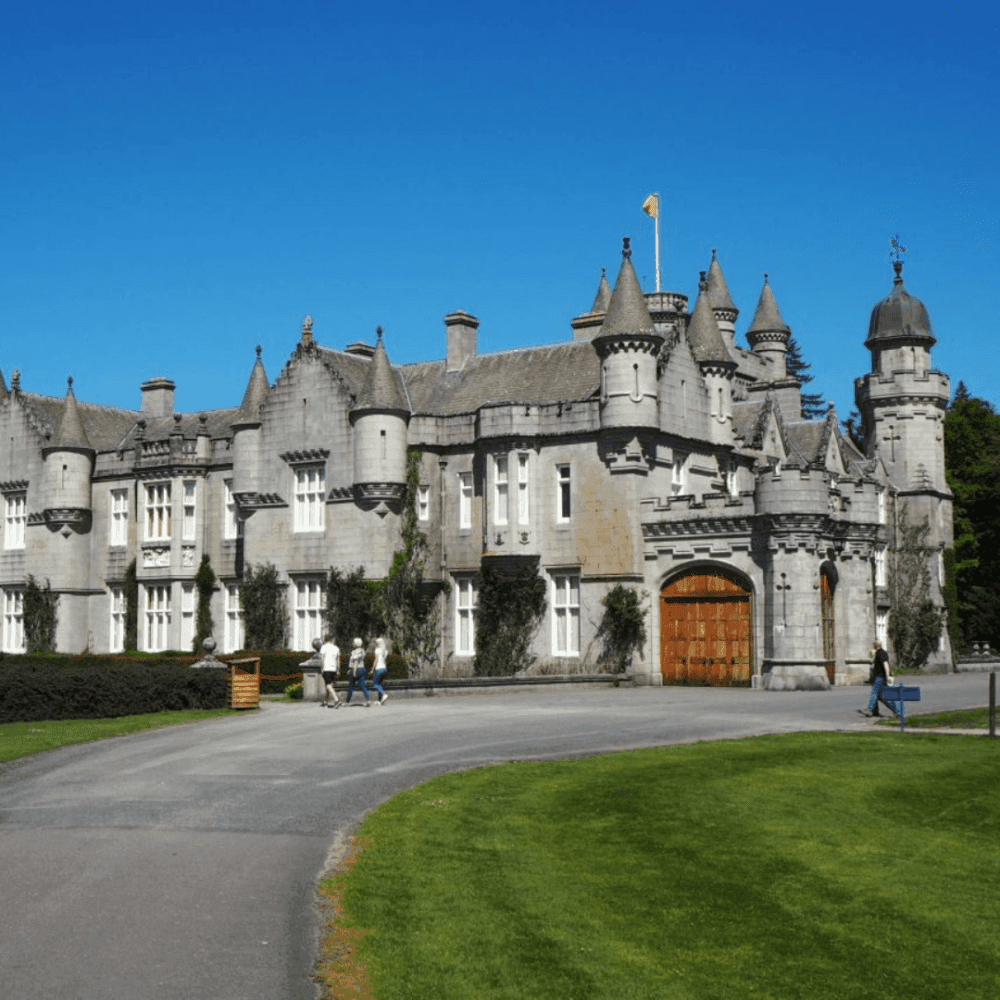 A large, historic stone castle with multiple turrets and spires, set against a clear blue sky. - Home Instead