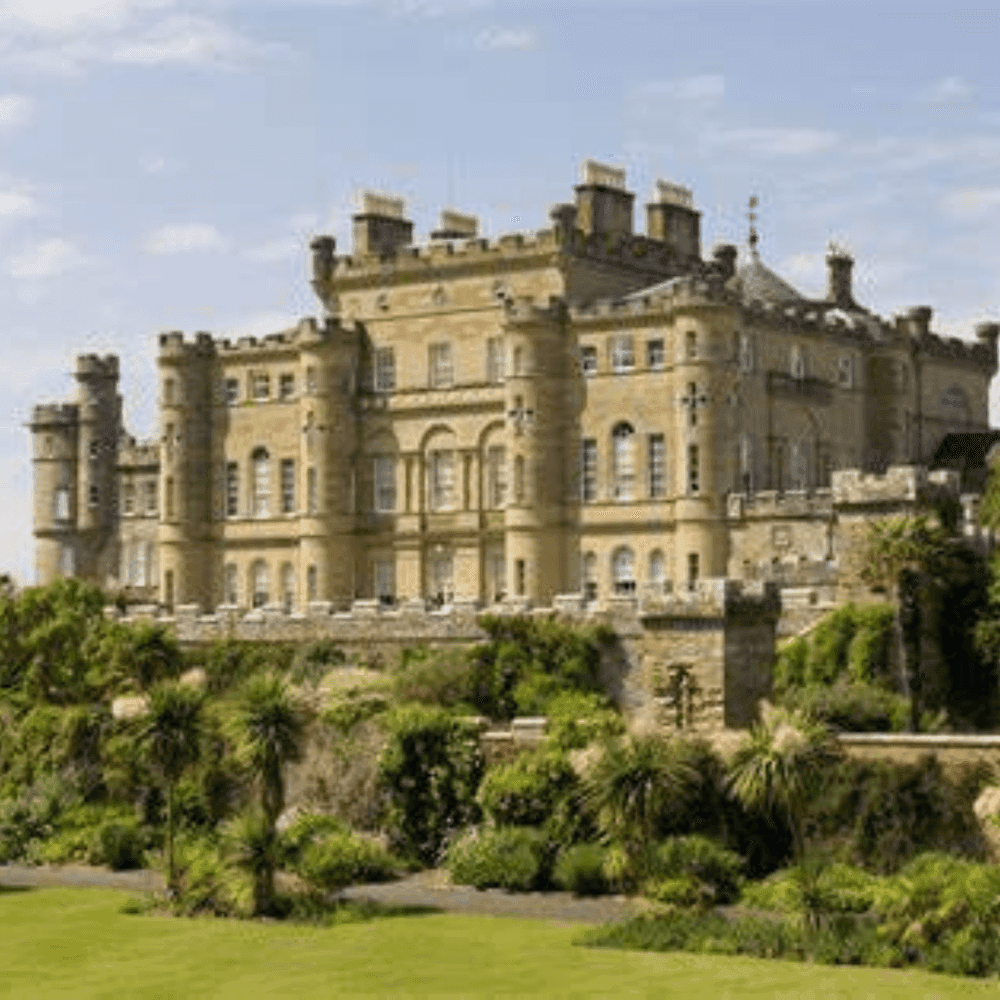 Historic castle with multiple towers surrounded by lush gardens and greenery on a sunny day. - Home Instead