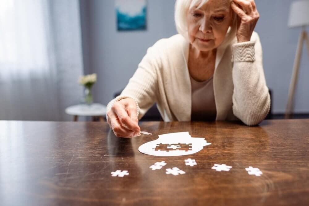 Elderly woman working on a brain-shaped jigsaw puzzle at a wooden table in a well-lit room. - Home Instead