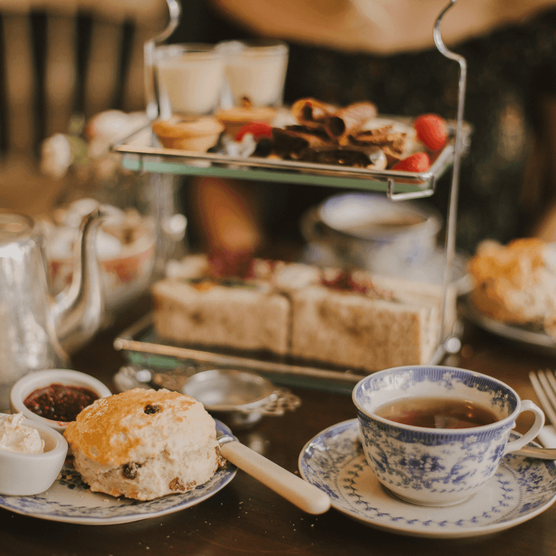 Elegant afternoon tea setup with scones, jam, clotted cream, sandwiches, pastries, and a cup of tea on a decorated table. - Home Instead