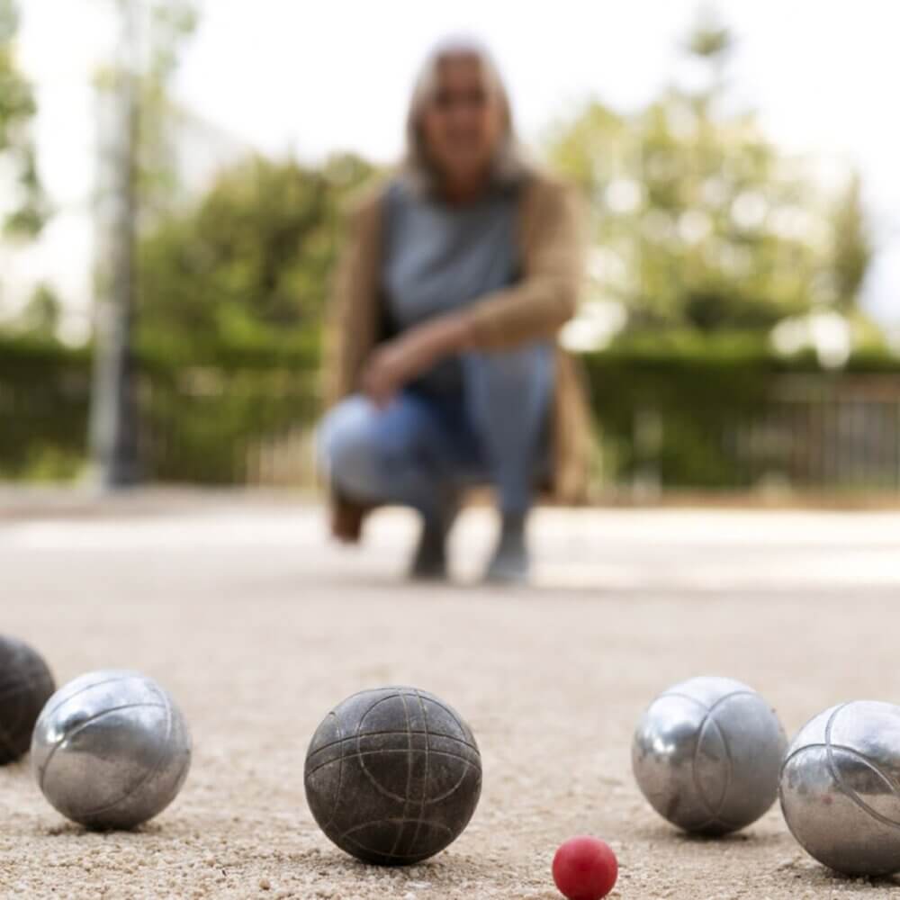 A person crouches in the background while several metal balls and a small red ball are scattered on the ground in the foreground. - Home Instead