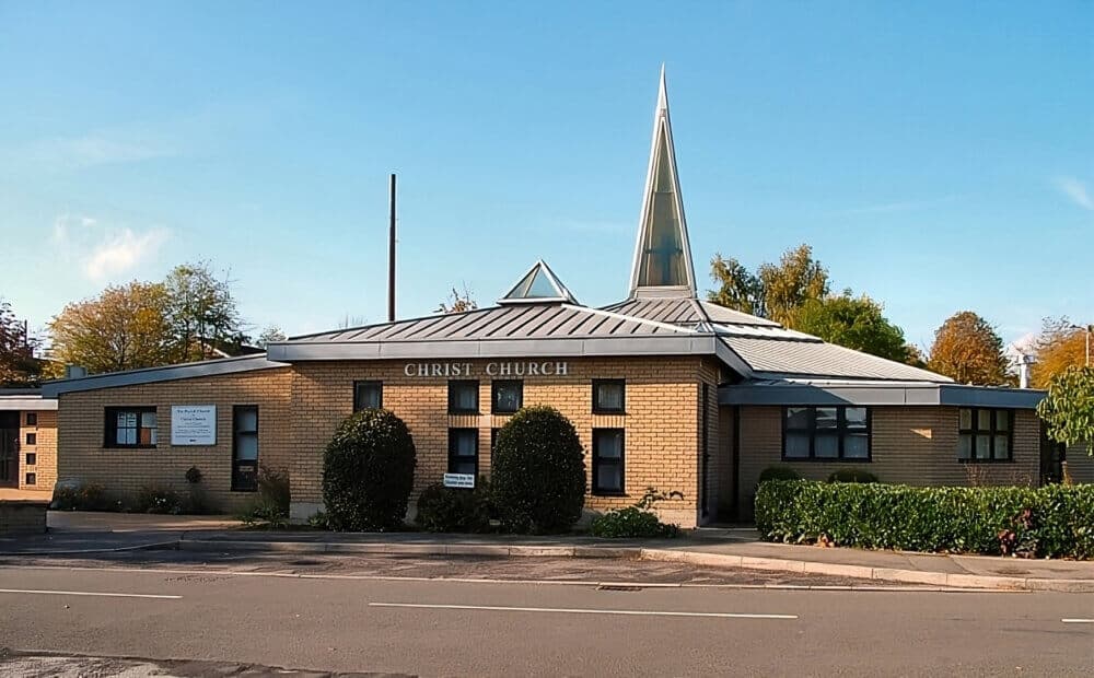 A modern brick church building with a spire and lush greenery on a sunny day. - Home Instead