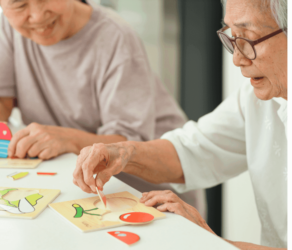 Two older adults joyfully engaging in a puzzle activity with brightly colored pieces at a table. - Home Instead