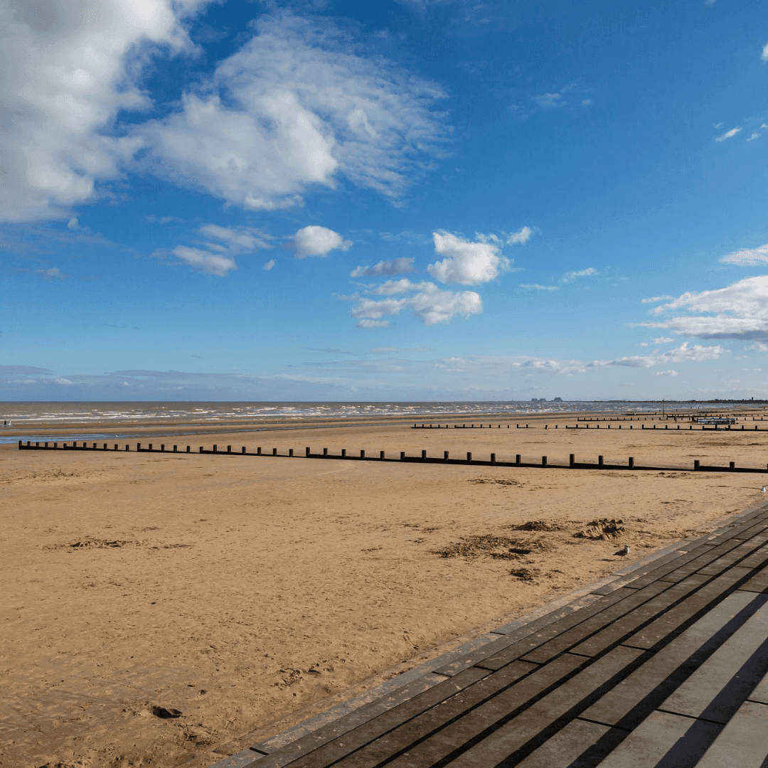 A sandy beach with wooden groynes under a partly cloudy blue sky. - Home Instead