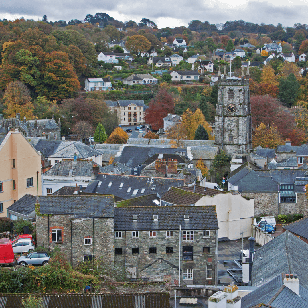 A small town with a mix of old and new buildings, prominent church tower, and autumn-colored trees on a hillside. - Home Instead