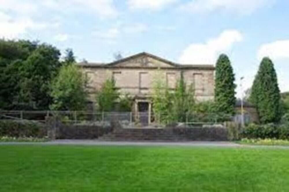 A large stone building with steps and greenery in front, surrounded by trees under a partly cloudy sky. - Home Instead