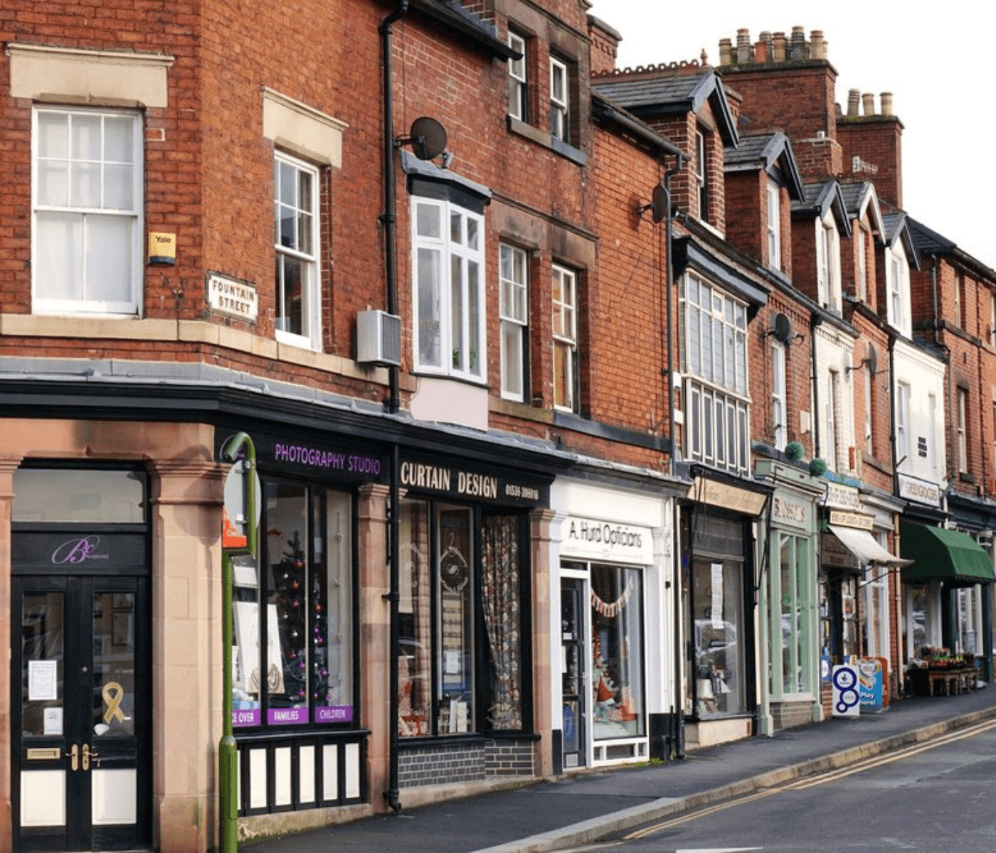 A street view showing various shops including a photography studio, curtain design shop, and optical store. - Home Instead