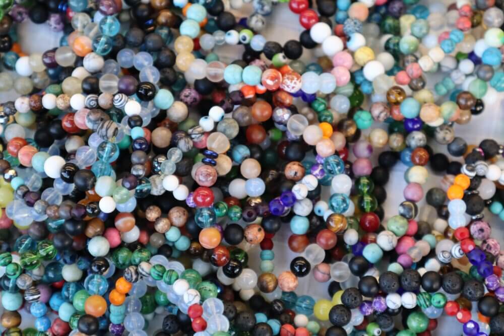 A close-up of numerous colorful beaded bracelets intertwined together in a pile. - Home Instead