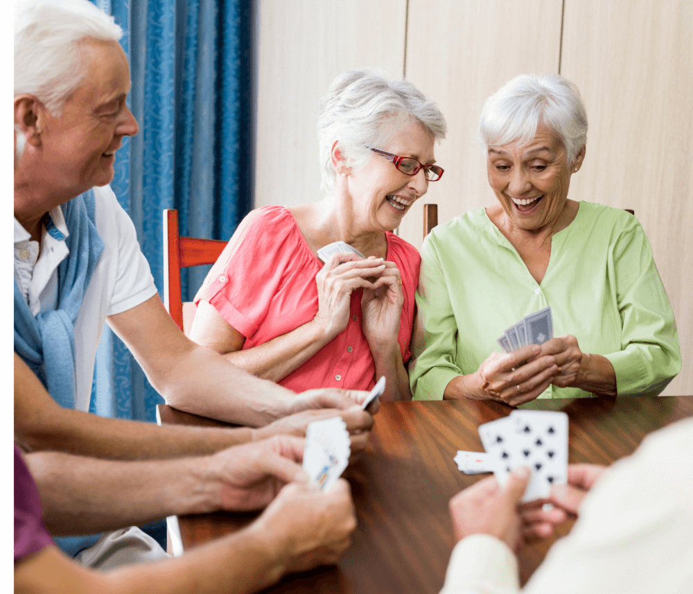 Four elderly people happily playing cards together at a table. - Home Instead